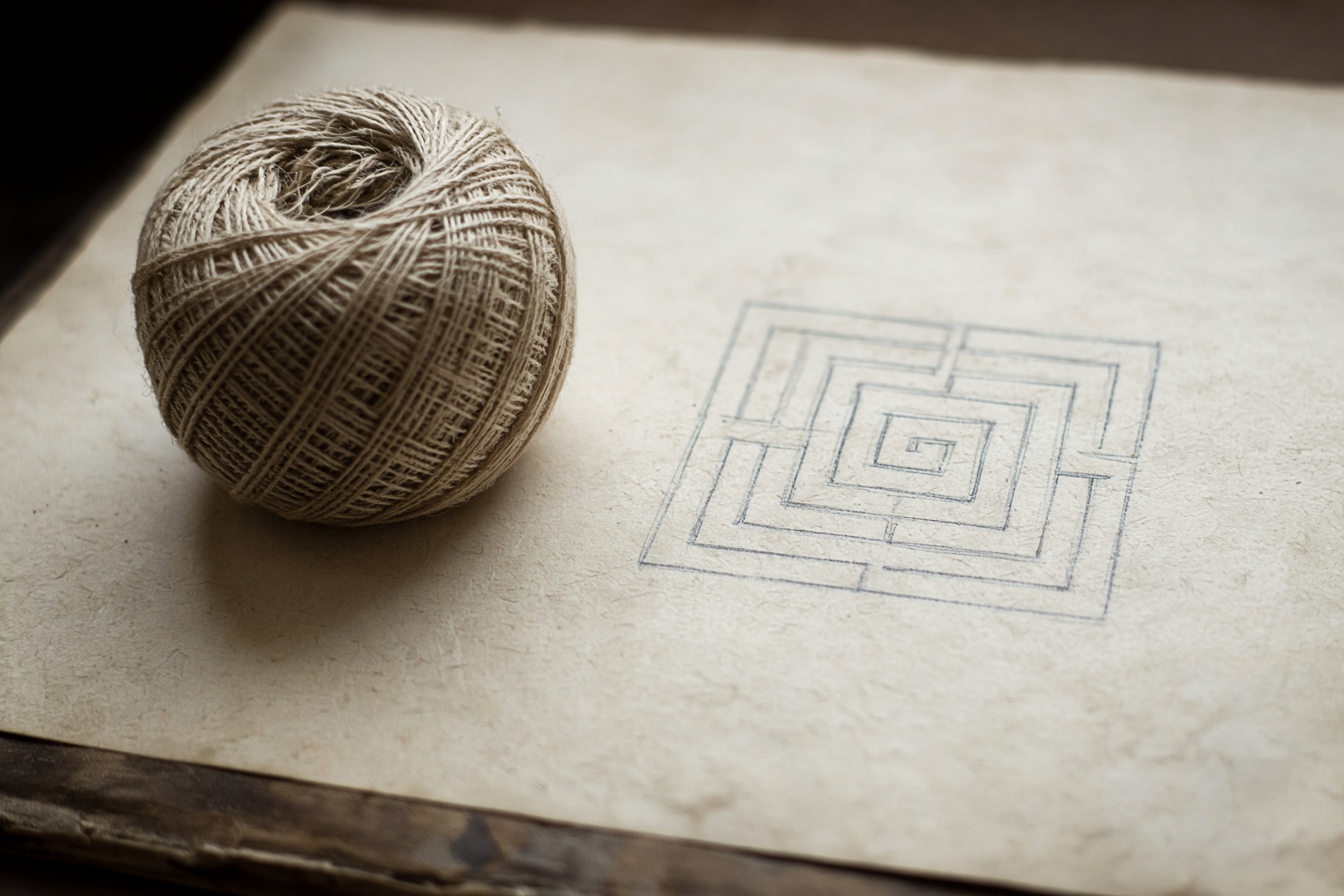 A ball of linen thread beside a faint labyrinth drawn on paper.
